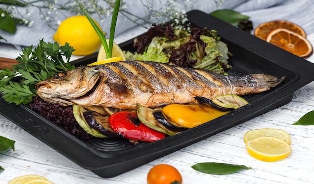 Free photo roasted fish garnished with lemon slices served with vegetables