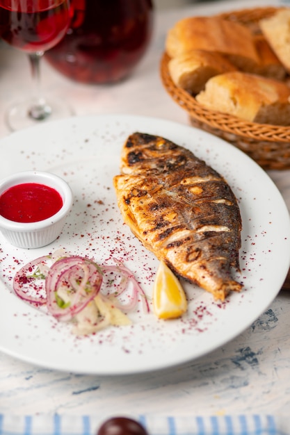 Free photo roasted grilled fish served with herbs, lemon,  onion salad and dip red tomato sauce.