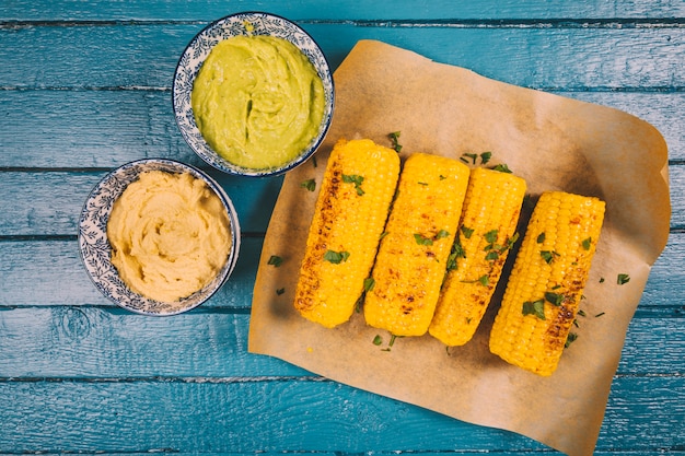 Free photo roasted organic sweet corn with guacamole and sauce on blue wooden table