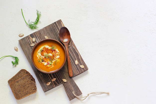 Free photo roasted pumpkin and carrot soup with cream, black pepper and pumpkin seeds , cutting board and fresh pumpkin slices, black bread