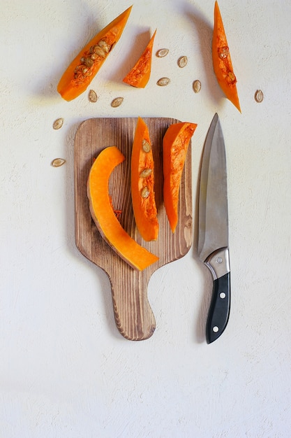 Roasted pumpkin and carrot soup with cream, black pepper and pumpkin seeds, cutting board and fresh pumpkin slices, black bread