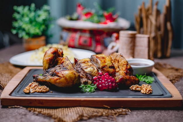 Free photo roasted stuffed chicken decorated with pomegranate and walnuts on a black board and rice in a white plate on a wooden table