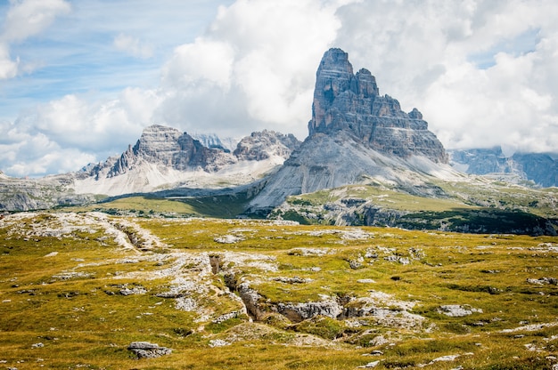 Rock formation on wide field grass under cloudy blue sky during daytime