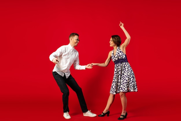 Free Photo rock n roll. old-school fashioned young woman dancing isolated on red studio background. young stylish man and woman.