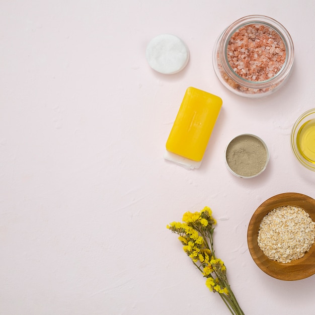 Rock salt; cotton pads; soap; oats; yellow limonium flower and cosmetics products on white concrete surface