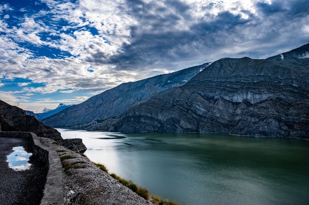 The rocky mountains and the green lake under the cloudy sky