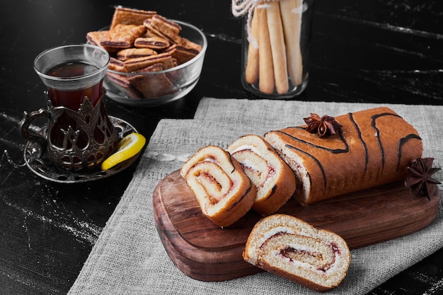 Roll cake sliced on a wooden board and served with a glass of tea.