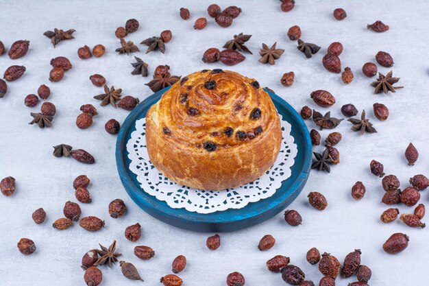 Roll with raisins on blue plate with rosehips and cloves. High quality photo