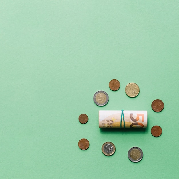 Rolled up euro bank note with coins on green backdrop