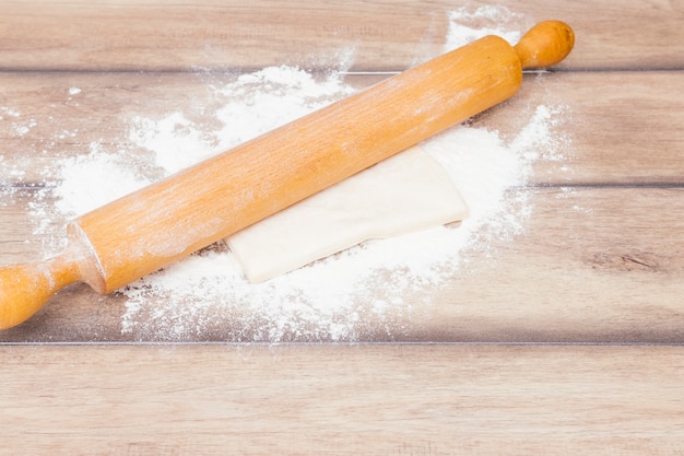 Free photo rolling pin over the kneaded dough and flour on wooden table