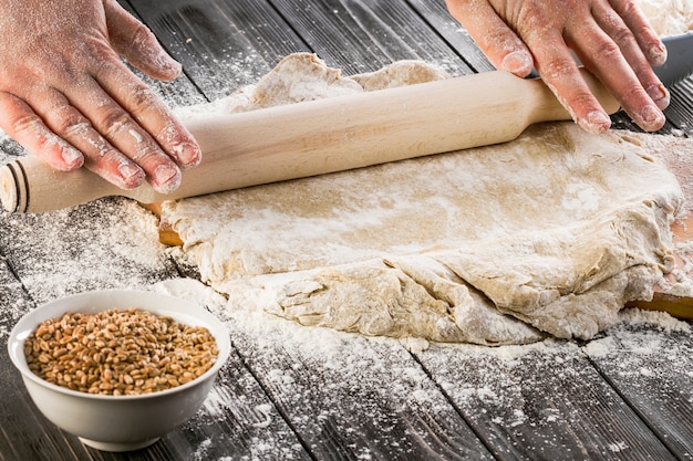 Free photo rolling the wheat dough with flour on the wooden table