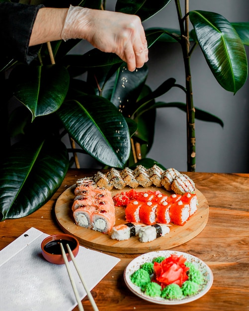 Rolls made from fish on the wooden round surface along with sticks and black sauce on the grey surface