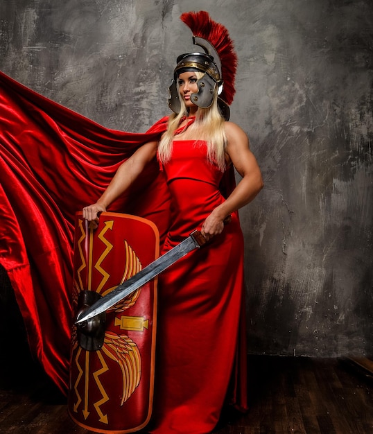 Free Photo roman warrior woman in red fluttering dress holds sword and shield.