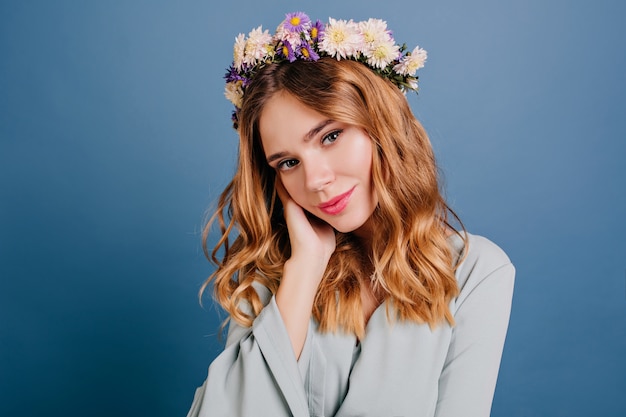 Free photo romantic blue-eyed woman with flowers in hair posing on dark wall