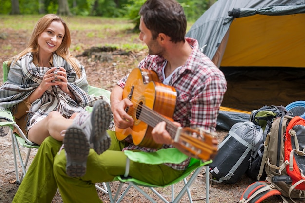 Romantic couple in a camping. Man playing the guitar.