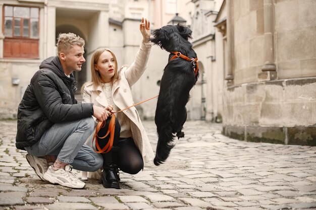 Romantic couple standing in the street on autumn time Man and woman petting a black dog on a street of old town Girl wearing beige coat and man black jacket