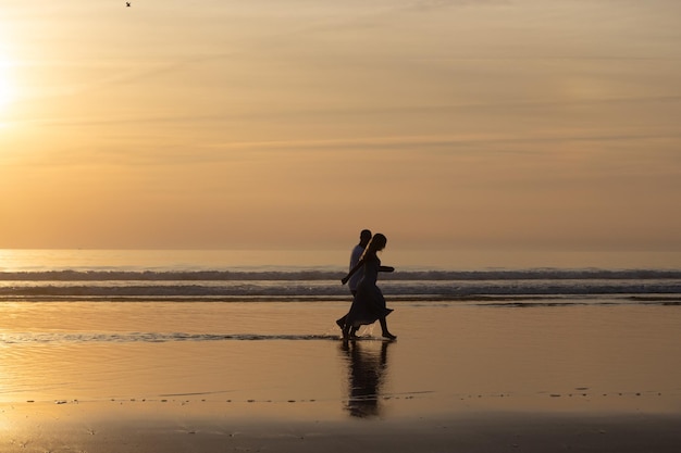 Free Photo romantic couple walking on beach at sunset. man and woman in casual clothes strolling along water at dusk. love, family, nature  concept