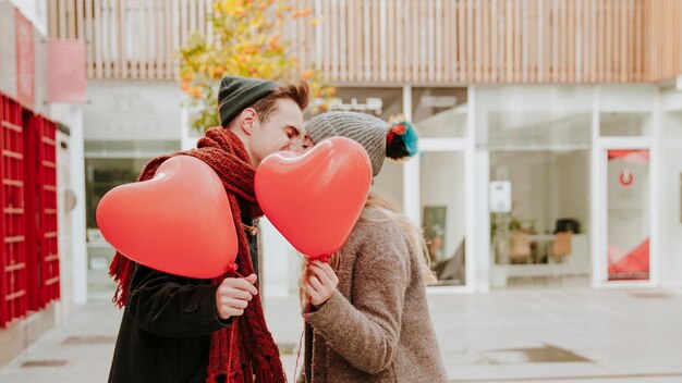 Free Photo romantic couple with balloons kissing on street