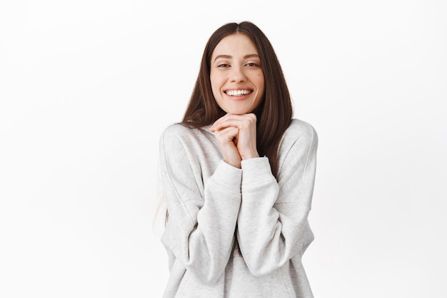 Romantic and cute girl looking with admiration and sympathy, admire something, watching beautiful lovely scene, resting head on hands and smiling, standing over white wall