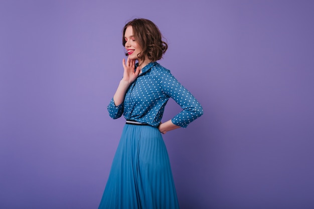 Free photo romantic female model with inspired face expression posing on purple wall. photo of jocund short-haired woman wears elegant long skirt.