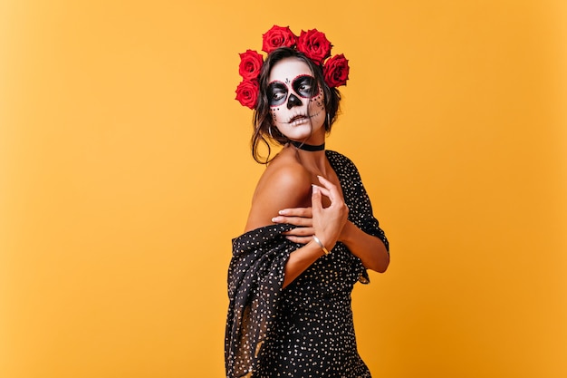 Free photo romantic girl gently holds falling dress. lady with make-up in form of skull for carnival mysteriously looks away.