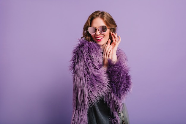 Free photo romantic girl in stylish purple outfit posing with shy smile in studio