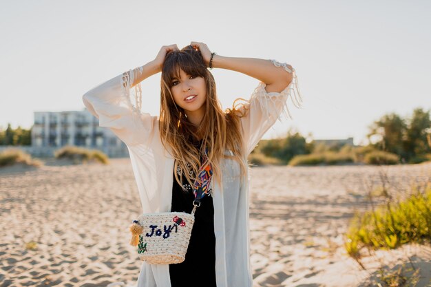 Romantic girl with long  brunette hair walking on the beach.   Bohemian style, straw bag , bright make up. Tropical mood. Sunset colors.