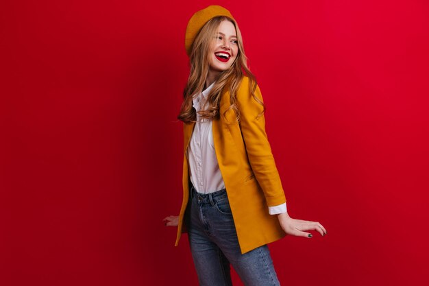 Romantic girl in yellow outfit posing with smile Studio shot of adorable french lady isolated on red background