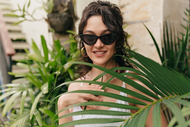 Romantic happy woman with short blond hair closed eyes and enjoying vacation in summer hot day on the island on wall of exotic plants