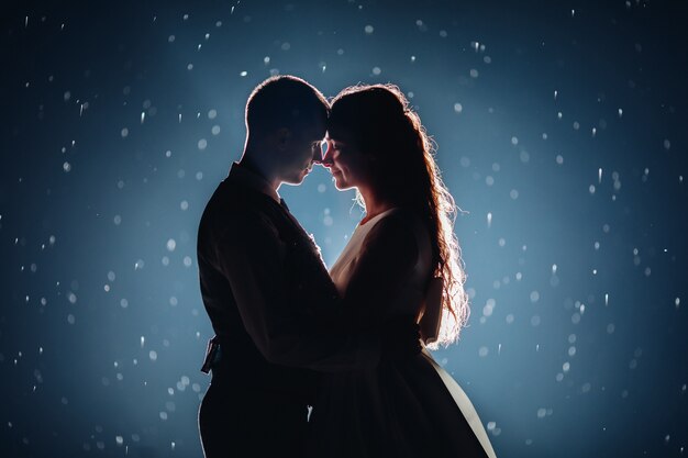 romantic just married couple hugging face to face against illuminated dark background with glowing sparkles around.