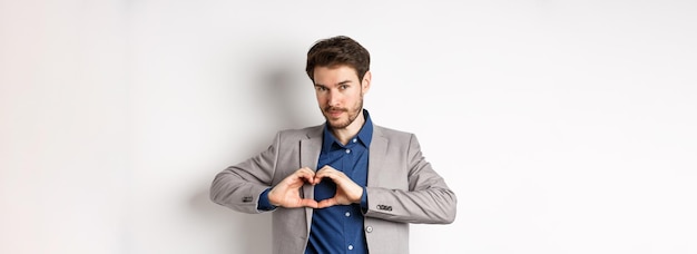 Free photo romantic man in suit showing heart sign and smiling love his girlfriend standing on white background