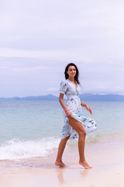 Romantic portrait of woman in long blue dress on beach by sea at windy day