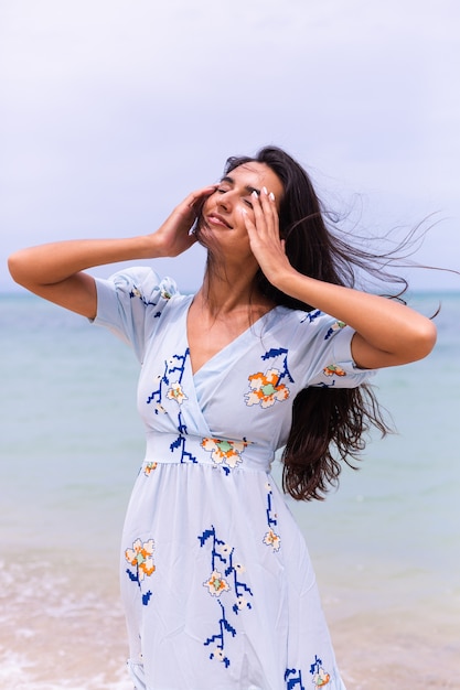 Romantic portrait of woman in long blue dress on beach by sea at windy day