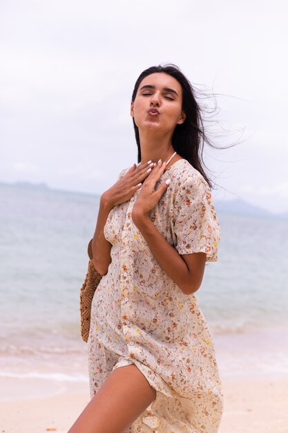 Romantic portrait of woman in long dress on beach at windy cloudy day.