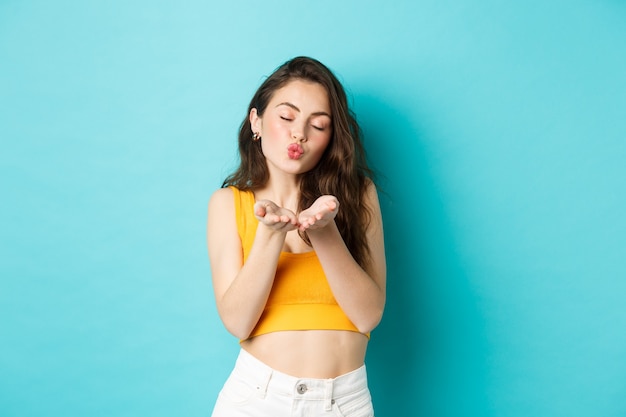 Romantic silly woman close eyes and pucker lips, blowing air kiss at you, standing dreamy against blue background