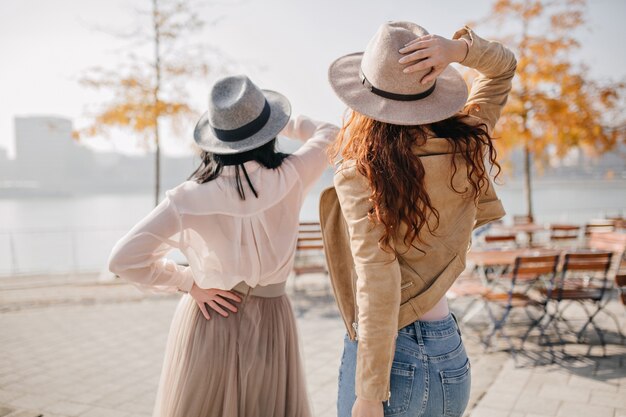 Romantic woman in gray hat decorated with ribbon wears elegant skirt in warm autumn day