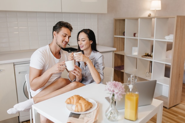 Romantic woman in white socks chilling with husband during breakfast and enjoying croissants