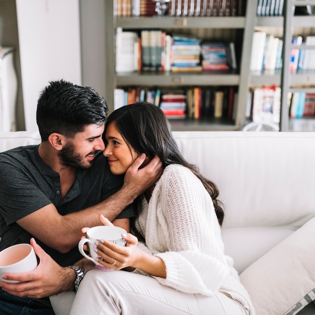 Romantic young couple sitting on sofa holding coffee cup