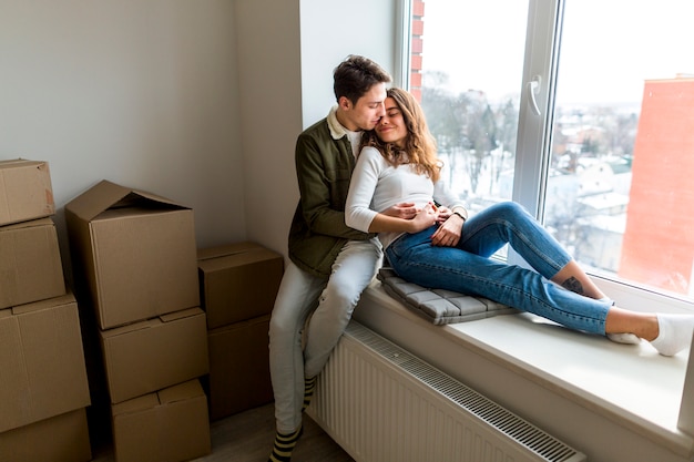 Free photo romantic young couple sitting on window sill in their new apartment