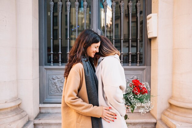 Romantic young girlfriends with flowers on street