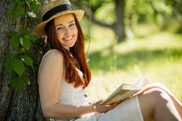 Romantic young lady in straw hat reading a book sitting in garden