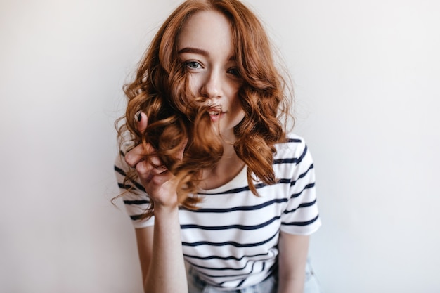 Free photo romantic young woman in casual clothes playing with her ginger hair. indoor photo of pleasant caucasian girl relaxing.