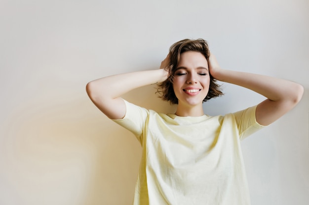 Free photo romantic young woman with short haircut posing with eyes closed.  amazing caucasian girl touching her head with smile.