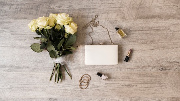 Free Photo rose bouquet; clutch; perfume; lipstick; nail varnish and hairbands on wooden background