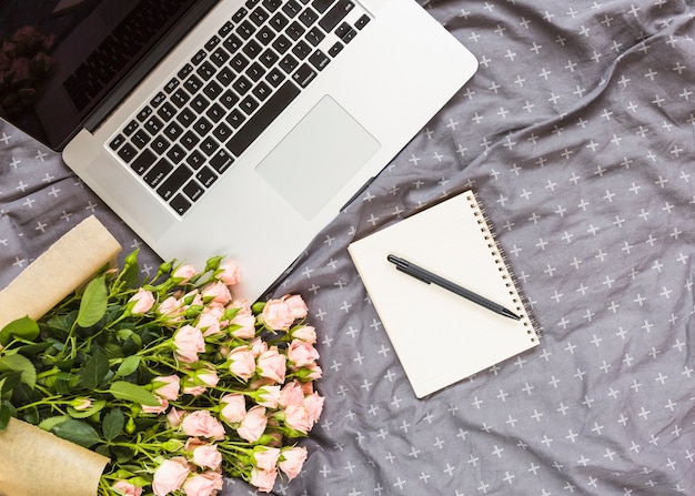 Free Photo rose bouquet; pen; spiral notepad and laptop on gray textile