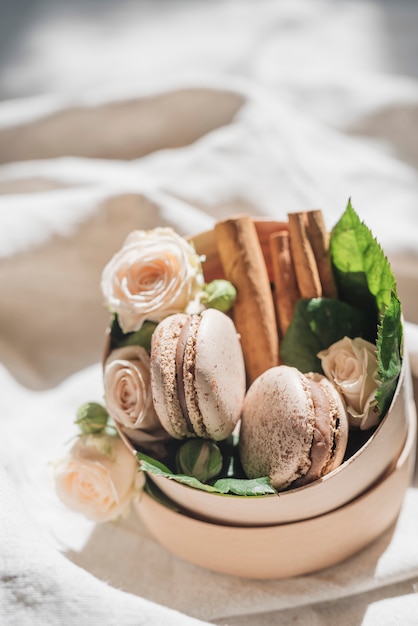 Free photo rose flowers with macaroons and cinnamon on container over the white cloth