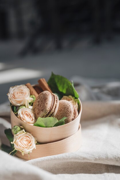 Roses and cinnamon with macaroons on container over the tablecloth