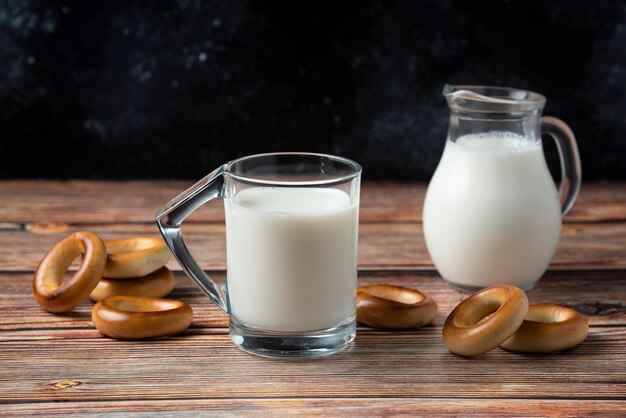 Round biscuits, glass mug and jug of milk on wooden table. 