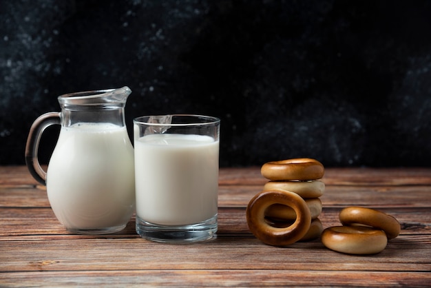 Round biscuits, glass mug and jug of milk on wooden table. 