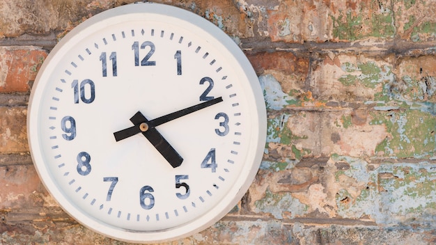 Free Photo round clock hanging on weathered brick wall